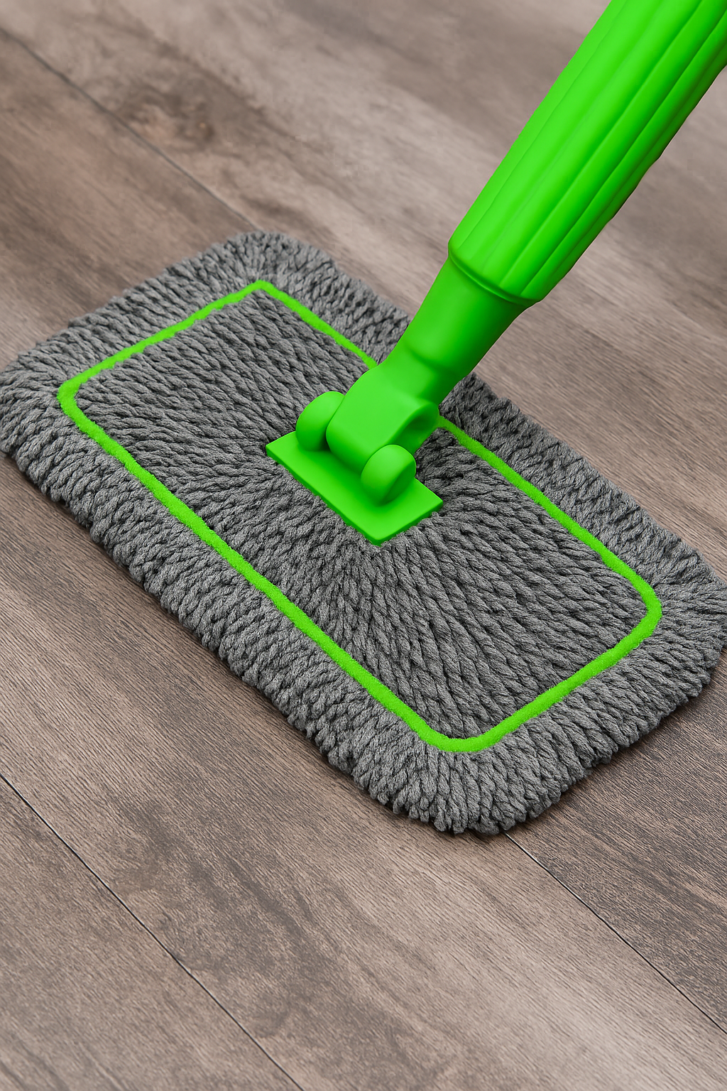 Gray microfiber mop with green handle on a wooden floor